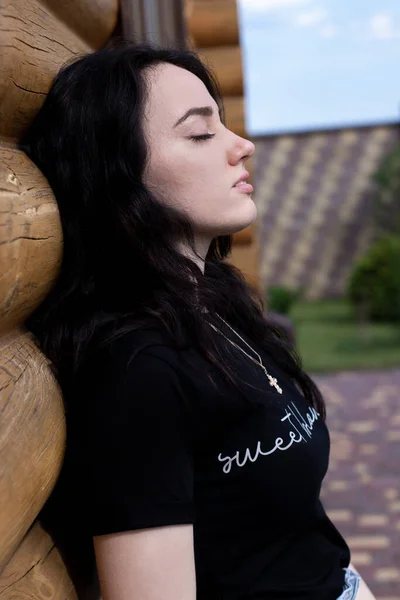 魅力的な若いですブルネット女性で黒tシャツとデニムショートパンツの横にある木のモダンな家 — ストック写真