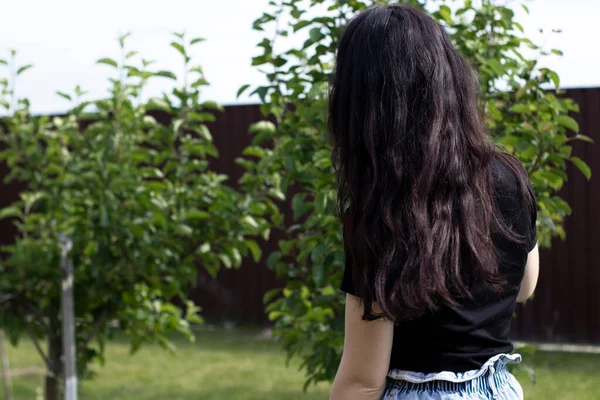 Charming young brunette woman in a black T-shirt and denim shorts. In the country, in the garden. — Stock Photo, Image