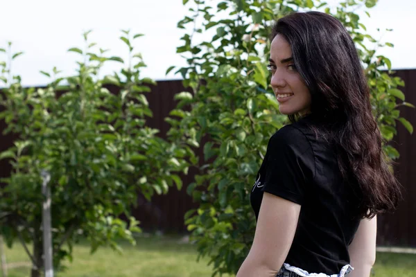 Fermecătoare tânără brunetă femeie într-un tricou negru și pantaloni scurți denim. În țară, în grădină . — Fotografie, imagine de stoc