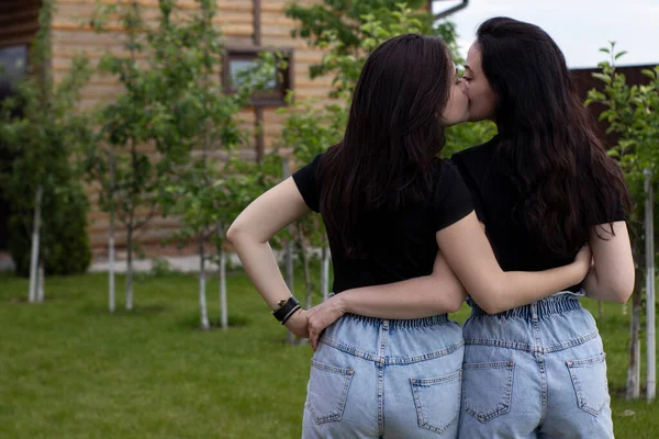 Twee jonge brunette vrouwen in een zwart T-shirt en denim shorts knuffelen. Zusters, vriendinnen. familie en vriendschap concept — Stockfoto