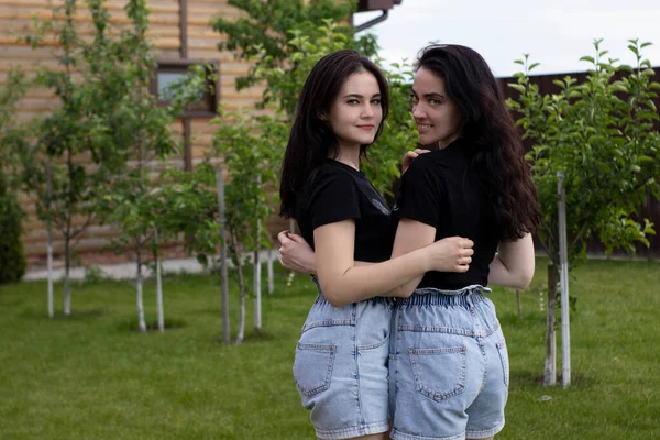 Two young brunette women in a black T-shirt and denim shorts hugging. Sisters, girlfriends.family and friendship concept — Stock Photo, Image