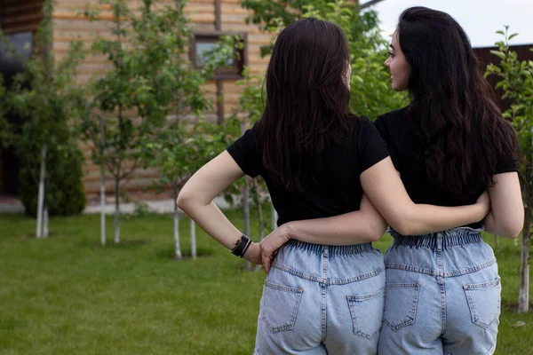 Dos mujeres morenas jóvenes con una camiseta negra y pantalones cortos de mezclilla abrazándose. Hermanas, novias.familia y concepto de amistad —  Fotos de Stock