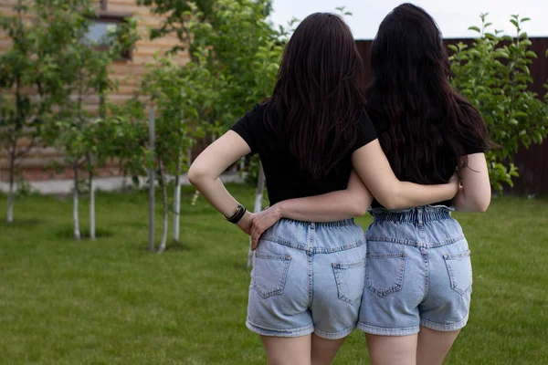 Dos mujeres morenas jóvenes con una camiseta negra y pantalones cortos de mezclilla abrazándose. Hermanas, novias.familia y concepto de amistad —  Fotos de Stock