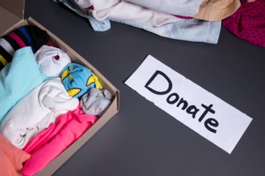 El yazısıyla siyah harflerle yazılmış bir bağış yazısı. Gri bir masa. Kıyafet bağışı konsepti üzerine giysi ve giysi yığını. Boşluğu kopyala