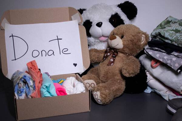 Donate sign handwritten with black letters. A box with clothes and a pile of clothes nearby on a grey table.clothes donation concept. copy space