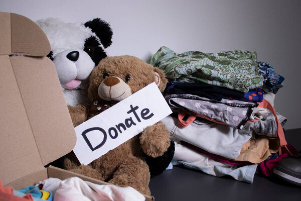 Donate sign handwritten with black letters. A box with clothes and a pile of clothes nearby on a grey table.clothes donation concept. copy space