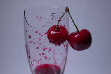 Kırık bir şampanya bardağında beyaz bir zemin üzerinde kiraz olan kırmızı bir sıvı kan damlası. İzole edilmiş