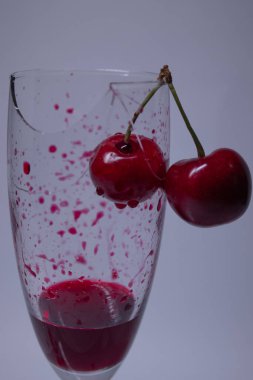 Kırık bir şampanya bardağında beyaz bir zemin üzerinde kiraz olan kırmızı bir sıvı kan damlası. İzole edilmiş