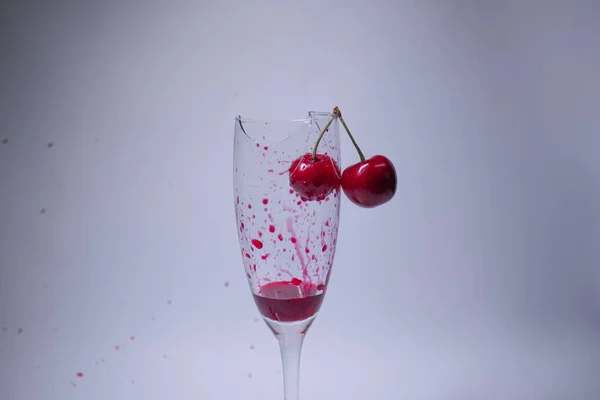 drops of red liquid - blood - in a broken champagne glass with a cherry on it on a white background. Isolated