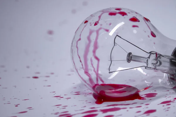 light bulb stained with red liquid - blood - on a white background in red drops. Copy space. Isolated