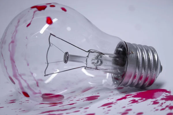 light bulb stained with red liquid - blood - on a white background in red drops. Copy space. Isolated