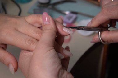 Manikür yapma süreci. Profesyonel manikürcünün elleri, kuafördeki tırnak derisini yüzüyor. Manikür ve tırnak temizliği kavramı. Güzellik konsepti Jel cilası, cila..