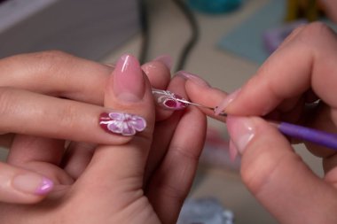 Manikür yapma süreci. Profesyonel manikürcünün elleri kapalı, tırnaklarına küçük çiçekler çiziyor. Manikür yapma kavramı. Güzellik konsepti Jel cilası, cila..