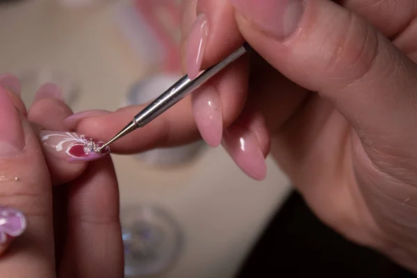 El proceso de hacer manicura. El primer plano de las manos de la manicura profesional, la aplicación de pequeñas piedras en las uñas. Concepto de hacer manicura. concepto de belleza. Esmalte de gel, goma laca . — Foto de Stock