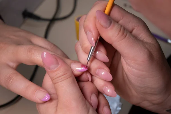 the process of doing manicure. Closeup of hands of professional manicurist, painting little flowers on nails. Concept of doing manicure. beauty concept. Gel polish, shellac.