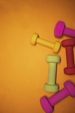 Turuncu arka planda parlak pembe, yeşil, kırmızı ve sarı küçük dambıllar. Spor konsepti.