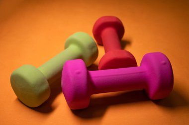 Turuncu arka planda parlak pembe, yeşil ve kırmızı küçük dambıllar. Spor konsepti.