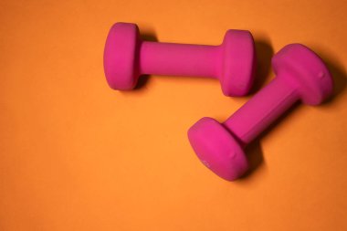 Turuncu arka planda parlak pembe küçük dambıllar. Spor konsepti.