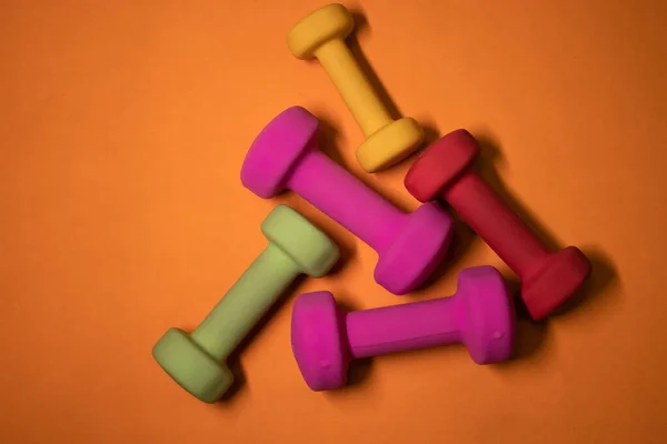 Λαμπερό ροζ, πράσινο, κόκκινο και κίτρινο μικρά αλτήρες σε πορτοκαλί φόντο. Αθλητική έννοια. — Φωτογραφία Αρχείου