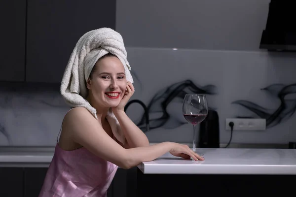 Attraktives brünettes Mädchen - in rosa Pyjama und mit weißem Handtuch auf dem Kopf - mit einem Glas Rotwein in der Küche — Stockfoto