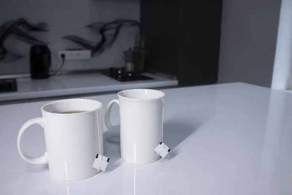 홍차를 탄 흰 컵 두 개와 회색 부엌에 있는 흰 탁자 위에찻 가방을 펴 놓고 있는 모습 — 스톡 사진