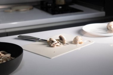 Üzerinde şampiyon mantarı olan beyaz plastik bir tahta kesiyor. yemek pişirme süreci
