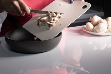 Kızlar beyaz bir masanın üstünde beyaz bir plastik tahta üzerinde şampiyon mantarı kesiyor. yemek pişirme süreci