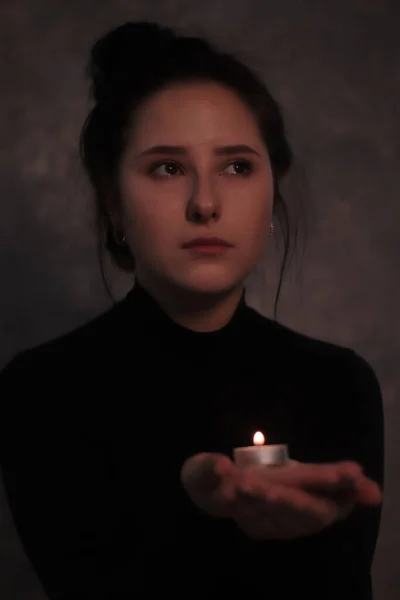 Portrait sombre d'une fille brune triste presque éclaté en larmes dans un col roulé noir tenant une bougie contre un mur gris — Photo