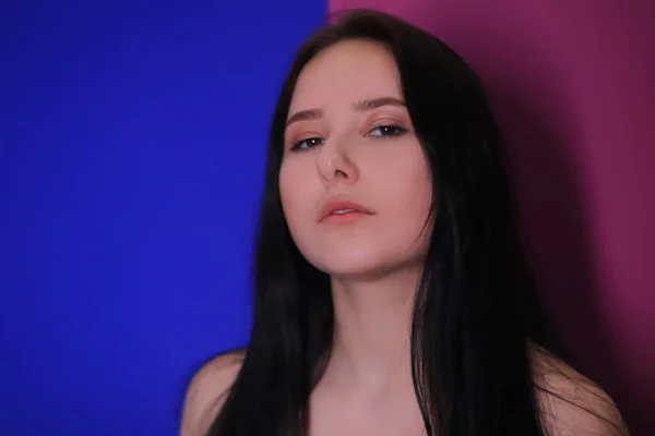 emotional pensive portrait of a pensive brunette girl on a pink-blue background