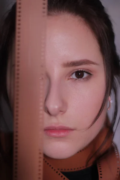 Retrato de una chica morena en un cuello alto negro envuelto en una tira de película carrete de película sobre un fondo de pared gris — Foto de Stock