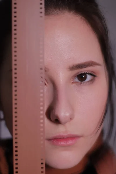 Retrato de una chica morena en un cuello alto negro envuelto en una tira de película carrete de película sobre un fondo de pared gris — Foto de Stock