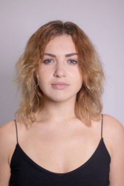 Siyah fanilalı, kıvırcık, sarışın, güzel bir kızın duygusal portresi.