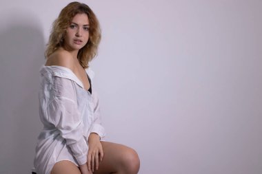 Güzel kıvırcık saçlı, siyah atlet ve beyaz gömlekli, yüksek bir bar sandalyesinde oturan sarışın bir kızın duygusal portresi.