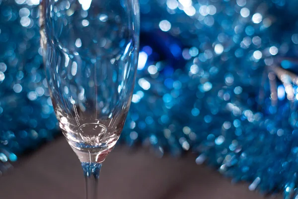 an engagement ring in a champagne glass near blue shiny tinsel for christmas tree. new years proposal theme