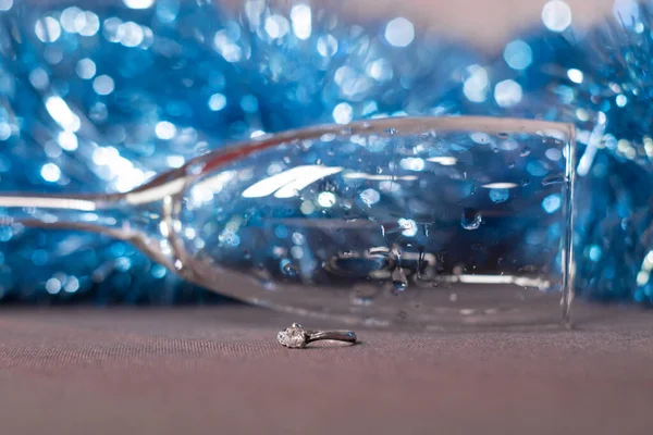 ブルーの光沢のあるティンセルの近くのシャンパングラスの婚約指輪クリスマスツリー。新年の提案テーマ — ストック写真