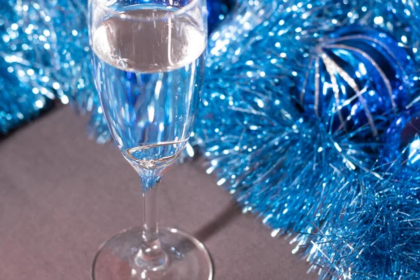 an engagement ring in a champagne glass near blue shiny tinsel for christmas tree. new years proposal theme