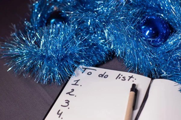 Een notitieboekje met de titel "Te doen lijst" met een pen in de buurt van een blauw glanzend koord voor kerstboom. Nieuwjaarsthema — Stockfoto