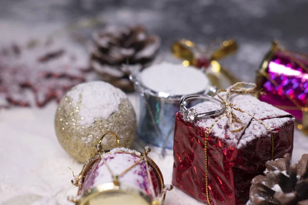 Joyas anillo de compromiso de plata junto a las decoraciones de Año Nuevo en la nieve. Árboles de Navidad, bolas, copos de nieve, regalos, conos. Humor de Navidad. Foto plana — Foto de Stock