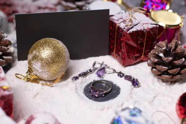 Purpurfarbener Schmuck - Ring und Ohrringe - neben Silvesterdekorationen im Schnee. Weihnachtsbäume, Kugeln, Schneeflocken, Geschenke, Zapfen. Weihnachtsstimmung. Flaches Foto — Stockfoto