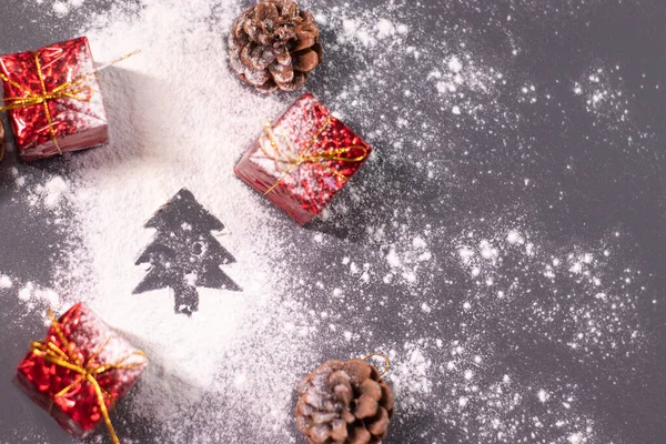 Kerstversieringen, geschenken en dennenappels in de sneeuw en het silhouet van een kerstboom. Kerststemming. Platte foto — Stockfoto