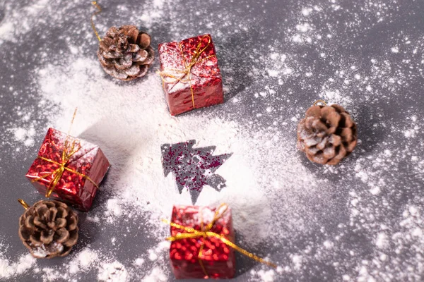 Kerstversieringen, geschenken en dennenappels in de sneeuw en het silhouet van een kerstboom. Kerststemming. Platte foto — Stockfoto