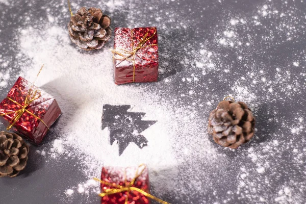 Kerstversieringen, geschenken en dennenappels in de sneeuw en het silhouet van een kerstboom. Kerststemming. Platte foto — Stockfoto