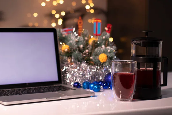 Fransız presinin yanında beyaz ekranlı dizüstü bilgisayar ve yeni yıl dekorasyonlarına yakın çay. Noel tema şablonu