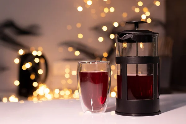 French press and tea in double-bottom glass on a background of golden yellow - orange bokeh — Stock Photo, Image