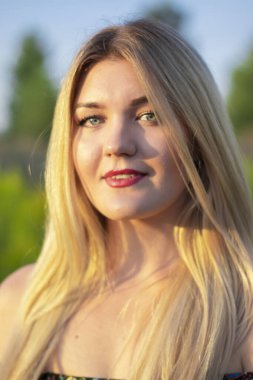 Açık renkli parlak bir portre. Tarlada çiçekli elbisesi olan çekici bir sarışın.