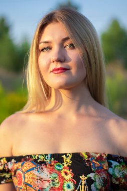 Açık renkli parlak bir portre. Tarlada çiçekli elbisesi olan çekici bir sarışın.