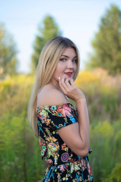 Overlight retrato brilhante de uma loira atraente encantadora em vestido florido no campo — Fotografia de Stock