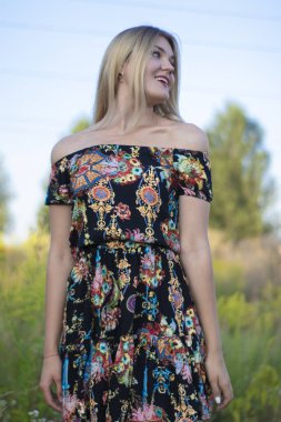 Açık renkli parlak bir portre. Tarlada çiçekli elbisesi olan çekici bir sarışın.