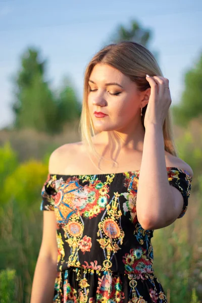 Overlight retrato brilhante de uma loira atraente encantadora em vestido florido no campo — Fotografia de Stock