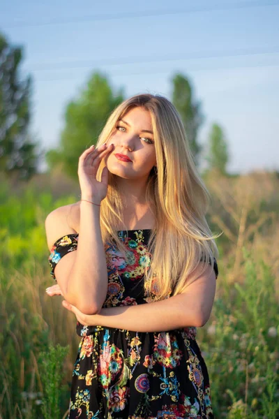 Overlight retrato brilhante de uma loira atraente encantadora em vestido florido no campo — Fotografia de Stock